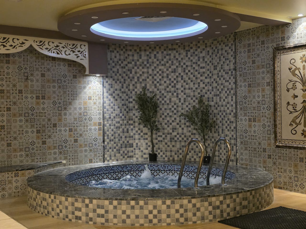 A serene indoor spa setting featuring a mosaic tiled jacuzzi with ambient lighting.